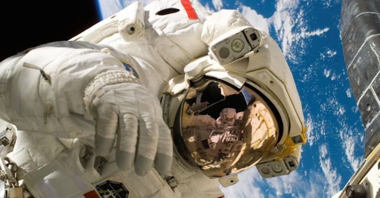 Science - This picture shows an american astronaut in his space and extravehicular activity suite working outside of a spacecraft. In the background parts of a space shuttle are visible. In the far background of the picture planet earth with it's blue color and white clouds is shown as well as a patch of black space.