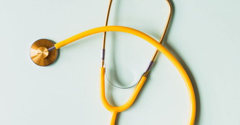 Diagnostics - Top view of yellow medical stethoscope placed on white surface during coronavirus pandemic