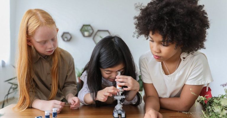 Biology - Concentrated multiethnic children in casual clothes watching in microscope while studying together