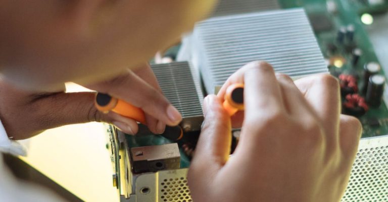 Scientific Technology - Crop of ethnic system administrator in uniform using screwdrivers and checking motherboard on electronic equipment during work in repair department